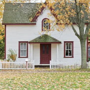 A white house featuring a red door, surrounded by a charming white picket fence.