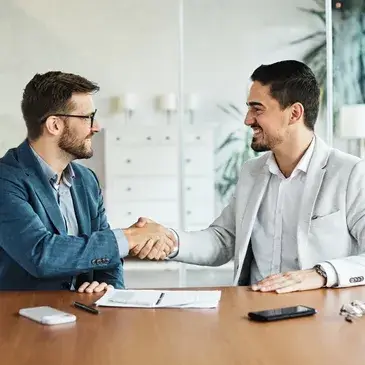 Two men shaking hands in a modern office setting, symbolizing a successful business agreement or partnership.