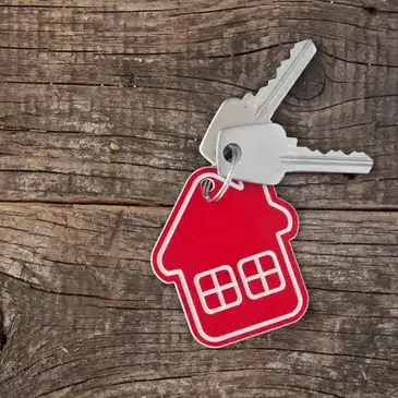 A red house key and matching key tag resting on a wooden table surface.